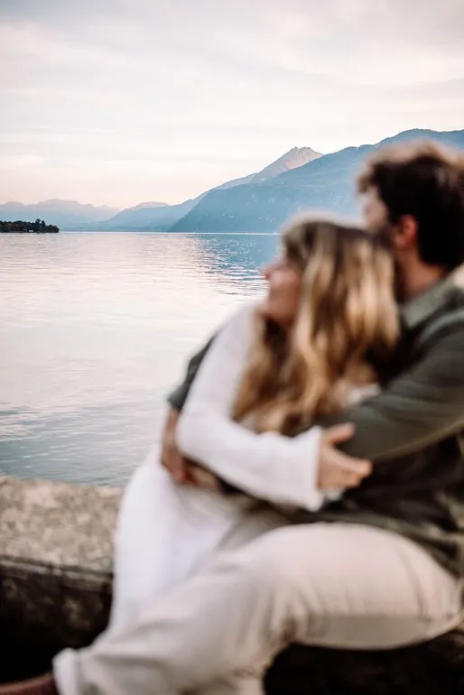 Couple amoureux s’enlaçant devant un lac au coucher du soleil, photographie romantique réalisée à Lyon par Noémie Herbert.