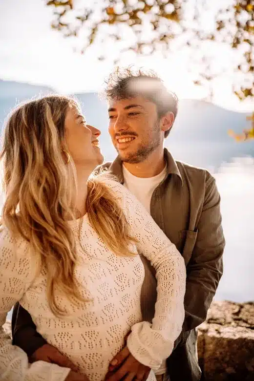 Couple amoureux s’enlaçant devant un lac au coucher du soleil, photographie romantique réalisée à Lyon par Noémie Herbert.