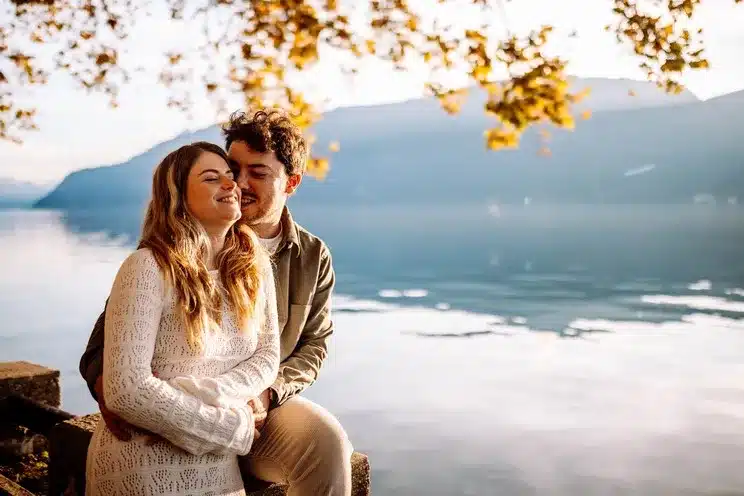 Couple amoureux s’enlaçant devant un lac au coucher du soleil, photographie romantique réalisée à Lyon par Noémie Herbert.