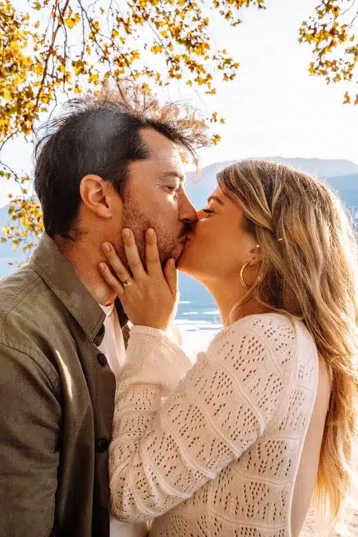 Couple amoureux s’enlaçant devant un lac au coucher du soleil, photographie romantique réalisée à Lyon par Noémie Herbert.