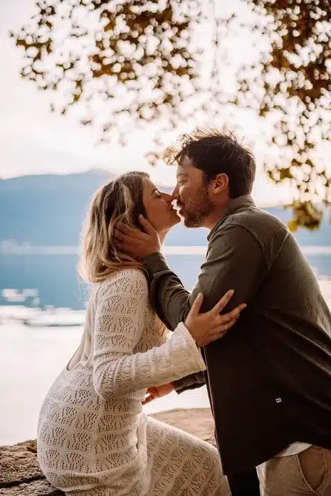 Couple amoureux s’enlaçant devant un lac au coucher du soleil, photographie romantique réalisée à Lyon par Noémie Herbert.