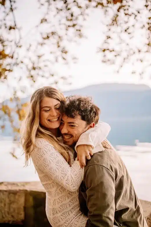 Couple amoureux s’enlaçant devant un lac au coucher du soleil, photographie romantique réalisée à Lyon par Noémie Herbert.
