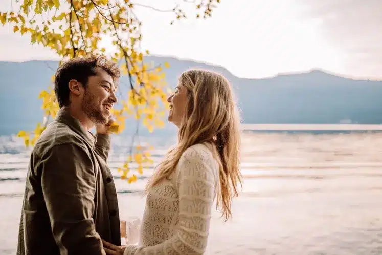 Couple amoureux s’enlaçant devant un lac au coucher du soleil, photographie romantique réalisée à Lyon par Noémie Herbert.