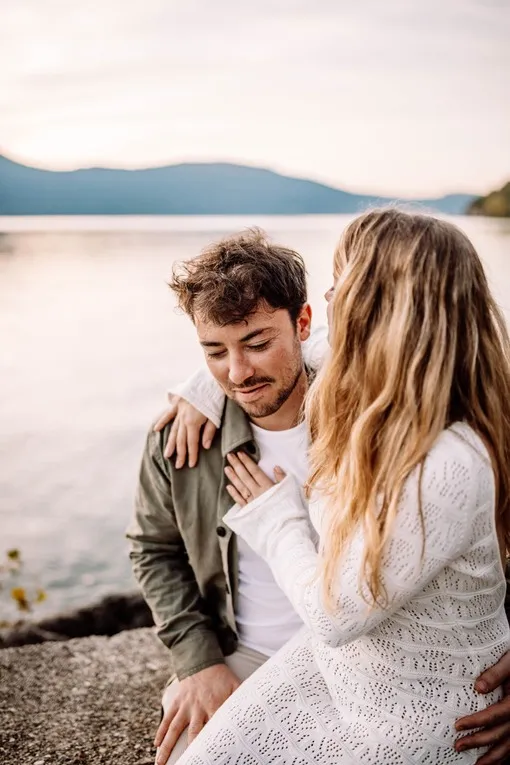 Couple amoureux s’enlaçant devant un lac au coucher du soleil, photographie romantique réalisée à Lyon par Noémie Herbert.