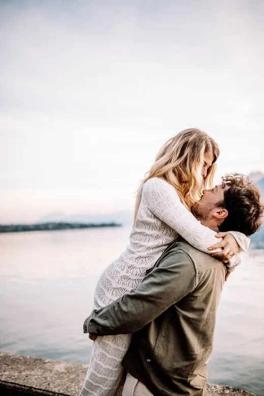 Couple amoureux s’enlaçant devant un lac au coucher du soleil, photographie romantique réalisée à Lyon par Noémie Herbert.